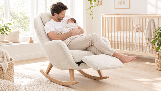 Father holding his sleeping newborn in a white teddy nursery rocker with the footrest out