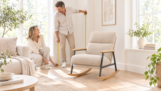 Couple measuring a bright living room corner with a tape measure next to a padded rocking chair