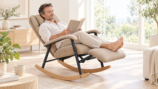 Man stretched out in a reclining rocker with the footrest up, reading in a bright living room