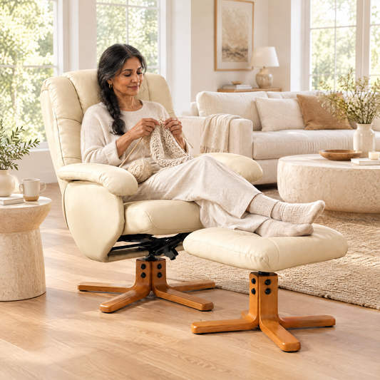 A South Asian woman with long dark hair in a loose braid in her mid 50s, knitting, in The Brighton faux leather swivel recliner + ottoman in a sunny living room