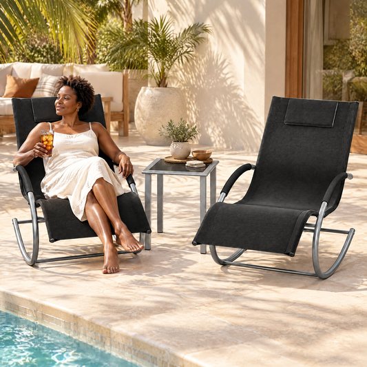 A Black woman with short natural curls in her mid 40s, holding a mug of tea and looking out the window, in The Lido set: 2 rocking sun loungers + side table in a poolside deck