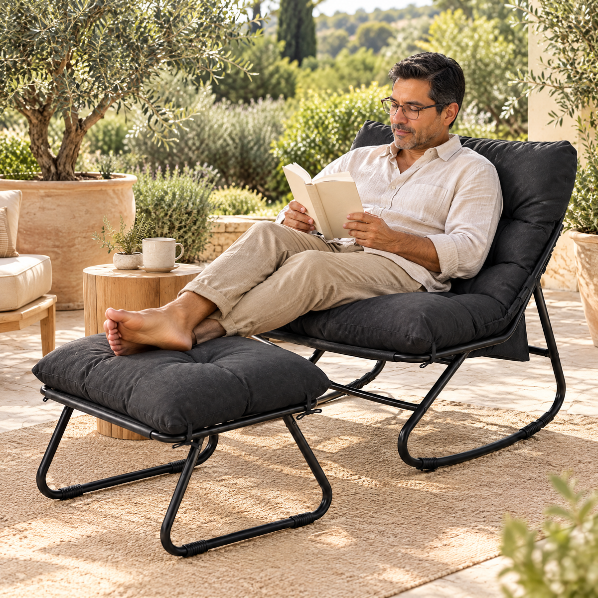 A Latino man with glasses and short dark hair in his early 50s, reading a paperback, in The Tidewater outdoor rocker + ottoman in a sunny stone patio